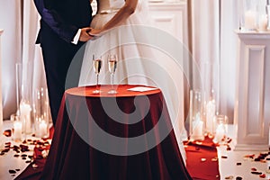 Bride and groom with champagne glasses on red table at evening w