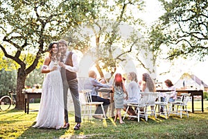 Bride and groom clinking glasses at wedding reception outside in the backyard.
