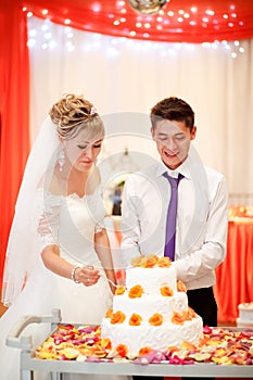 Bride and groom cut the cake at a banquet with orange flowers in decoration.