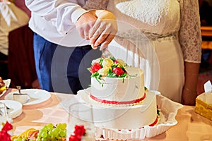 Bride and groom cut wedding cake together with white and red flowers