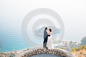 The bride and groom embrace on the observation deck overlooking the island of Sveti Stefan