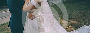 Bride and groom embrace in the park, the bride has a very long veil to the ground, the groom is dressed in a dark blue suit