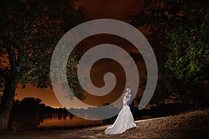 Bride and groom embracing by the lake under the stars.