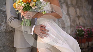 The bride and groom are embracing at the stone wall of an old house, close-up