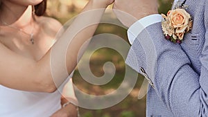 The bride and groom exchange wedding rings against a background of green nature. The groom puts the ring on the arm of