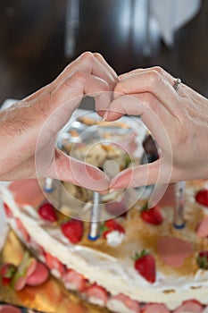 Bride and groom in front of cake making a heart with hands