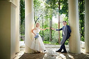 Bride and groom in gazebo near the white columns in a sunny summer day in the city park