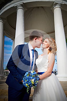 Bride and groom in gazebo near the white columns in a sunny summer day in the city park