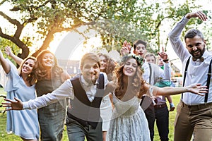 Bride, groom, guests posing for the photo at wedding reception outside in the backyard.