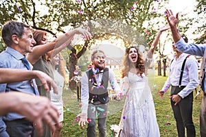Bride, groom and guests throwing confetti at wedding reception outside.