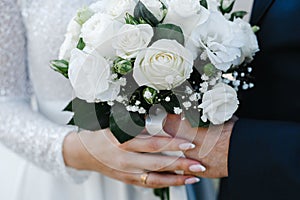 Bride and groom hold a bouquet of brides from white roses