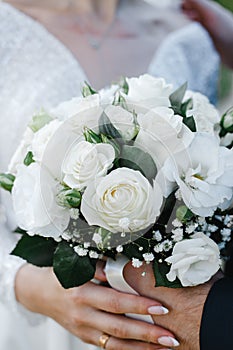 Bride and groom hold a bouquet of brides from white roses