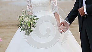 The bride and groom hold hands. The bride has a bouquet in her hands.