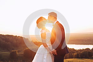 The bride and groom hold hands and kiss in nature during sunset