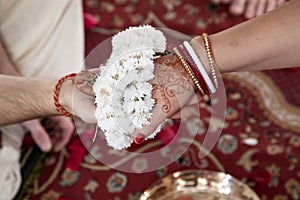 The bride and groom hold hands tied with a garland of white flowers. Beautiful traditional Indian wedding ceremony