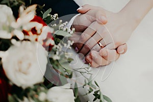 Bride and groom hold hands during a wedding ceremony in front of a wedding bouquet