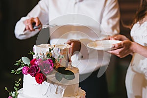 The bride and groom hold a plate and knife and cut the wedding cake with flowers and white cream