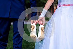 The bride and groom hold the shoes of the bride between themselves and hold hands with their little fingers. Wedding in detail