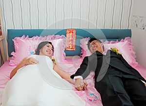 Bride and groom hold their hand and lay on the bed