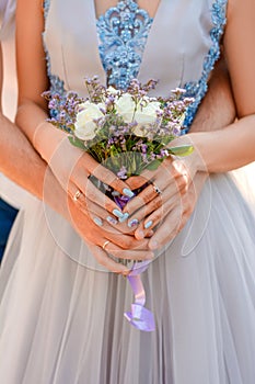 The bride and groom hold in their hands a cute wedding bouquet closeup of white roses and small purple flowers.