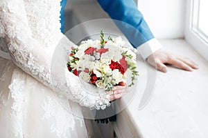 Bride and groom holding bridal bouquet close up. red and white roses, freesia, brunia decorated in composition