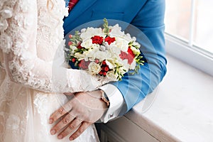 Bride and groom holding bridal bouquet close up. red and white roses, freesia, brunia decorated in composition