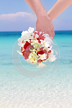 Bride and groom holding bridal bouquet on natural sea background