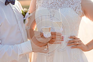 Bride and groom are holding and clinking wedding glasses with champagne close-up.