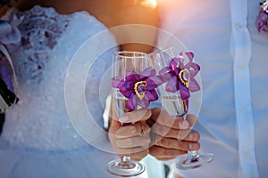 Bride and groom holding glasses of champagne in their hands, close-up. Glasses decorated with ribbons. Newlyweds clinking glasses