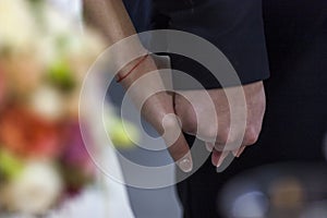 Bride and groom holding hands during a ceremony of background of blurred bridal bouquet. grain effect. lovers of newlyweds hand in