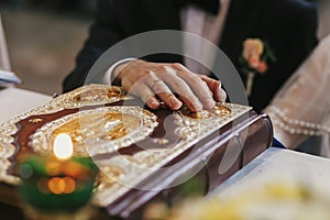 bride and groom holding hands on golden bible on holy altar during wedding ceremony in church, exchanging oaths. spiritual moment