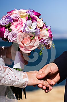 Bride and groom holding hands together on a sea coast.