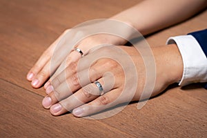 Bride and groom holding hands with wedding ring on wooden table