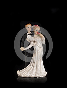 Bride and groom holding an old cake topper on a black background. Figurines for a wedding cake