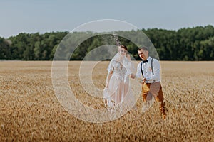 Bride and groom holding wedding champagne glasses on the background of wheat field. Happy wedding couple in wheat field