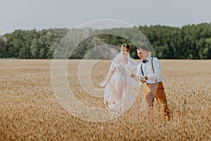 Bride and groom holding wedding champagne glasses on the background of wheat field. Happy wedding couple in wheat field