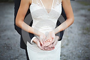 Bride and groom holding wedding rings. Married couple on grey background. Happy newlyweds.