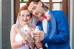 Bride and groom are holding a white doves in his hands.