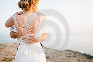The bride and groom hug on the rocks by the sea against the backdrop of the mountains and the island of Mamula, back