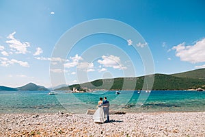 bride and groom are hugging on the beach of the Mamula island against the backdrop of the ancient fortress