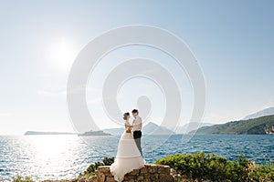 bride and groom are hugging on the beach of the Mamula island against the backdrop of the Arza fortress