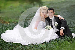 Bride and groom hugging and looking in the eyes of one another sitting at a green grass