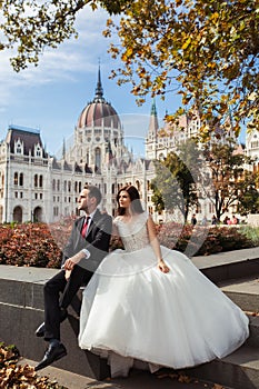 Bride and groom hugging in the old town street. Wedding couple sit in Budapest near Parliament House. Caucasian happy