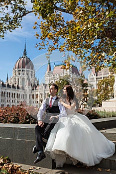 Bride and groom hugging in the old town street. Wedding couple sit in Budapest near Parliament House. Caucasian happy