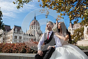 Bride and groom hugging in the old town street. Wedding couple sit in Budapest near Parliament House. Caucasian happy