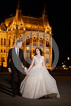 Bride and groom hugging in the old town street. Wedding couple walks in Budapest near Parliament House in night. Happy