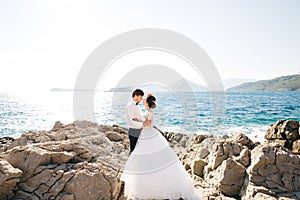 Bride and groom are hugging on the rocky beach of the Mamula island against the background of the Arza fortress