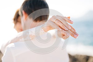 Bride and groom are hugging on the rocky beach of the Mamula island, the bride put her hands on the groom`s shoulders