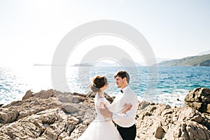 Bride and groom are hugging on the rocky beach of the Mamula island near Arza fortress