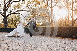 Bride and groom joyfully running together down a path on their wedding day, diverse couple holding hands and eloping